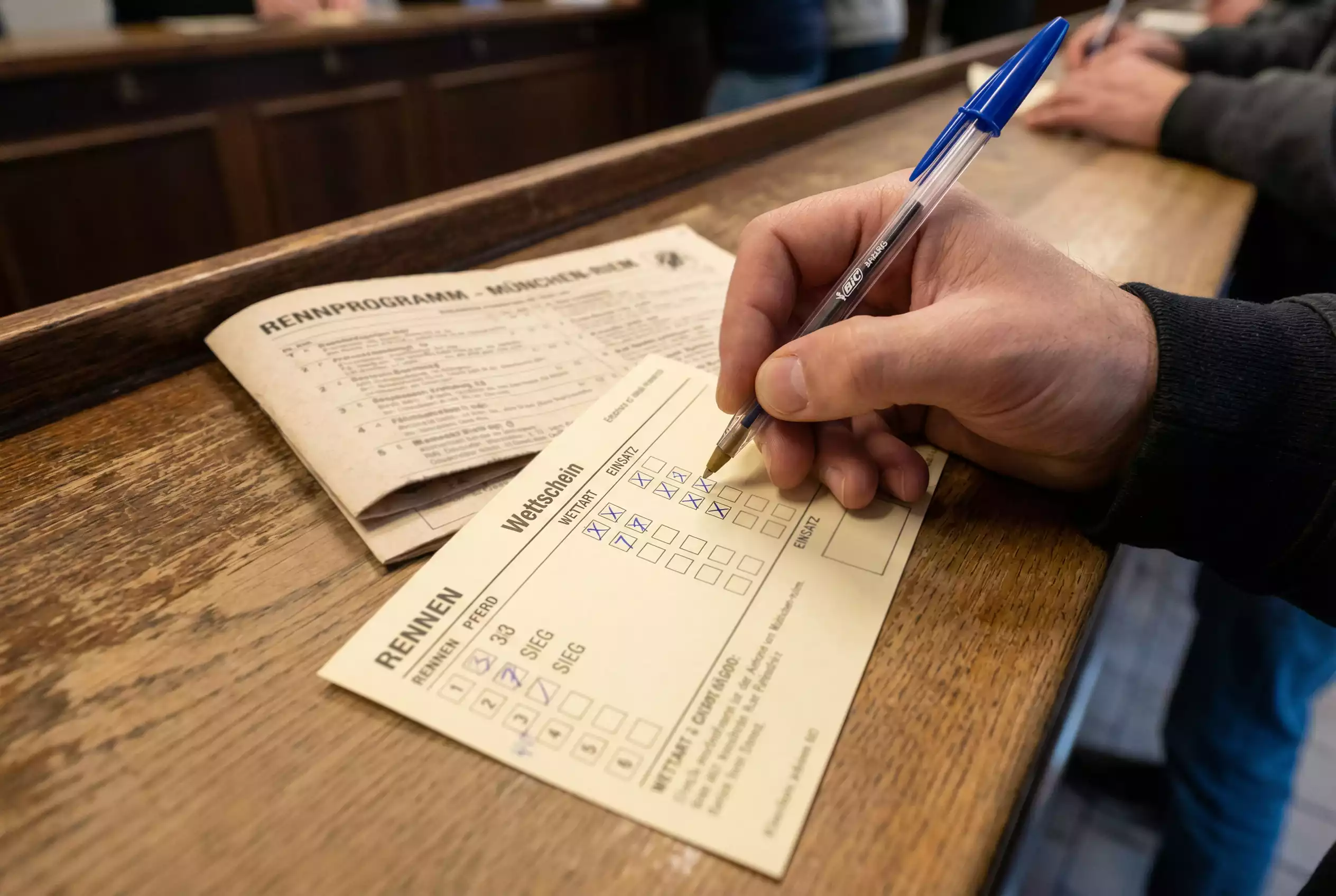 Wettschein ausfüllen – Hand füllt Wettschein mit Kugelschreiber auf der Rennbahn aus